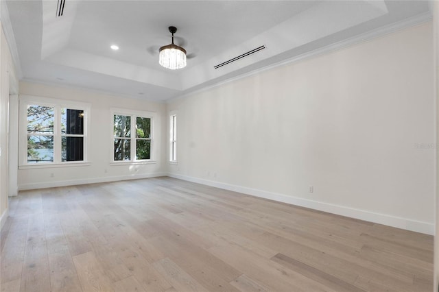 empty room with a notable chandelier, ornamental molding, light hardwood / wood-style floors, and a raised ceiling