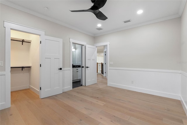 unfurnished bedroom with a walk in closet, ornamental molding, a closet, ceiling fan, and light hardwood / wood-style floors