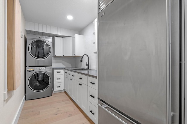 clothes washing area with cabinets, stacked washer / dryer, sink, and light hardwood / wood-style flooring