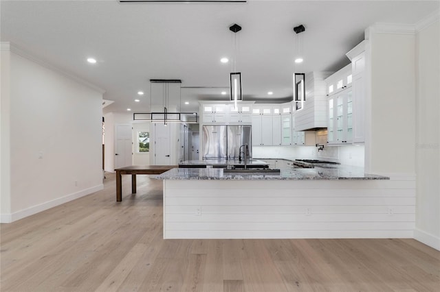 kitchen with stainless steel refrigerator, decorative light fixtures, white cabinets, light stone counters, and kitchen peninsula