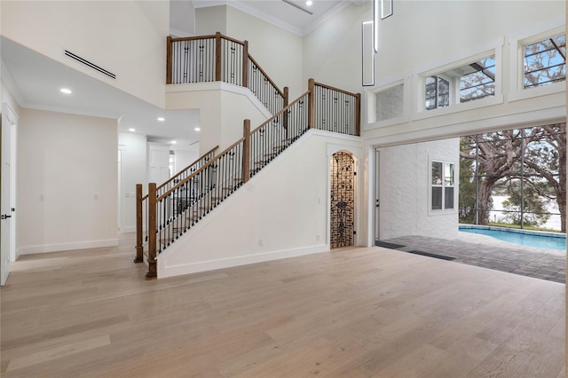 foyer entrance with crown molding, light wood-type flooring, and a high ceiling