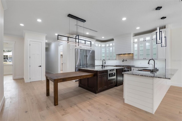 kitchen featuring a sink, built in appliances, light wood-style floors, and light stone countertops