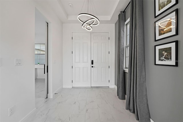 foyer entrance featuring a tray ceiling and a chandelier