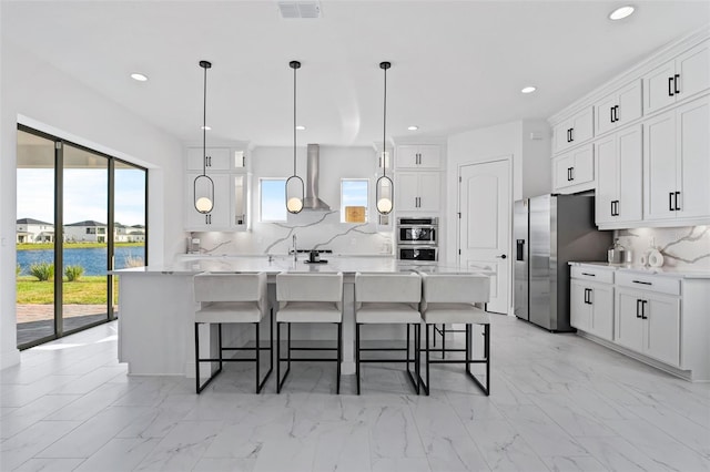 kitchen featuring white cabinets, a large island with sink, backsplash, and a water view