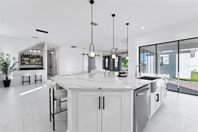 kitchen with pendant lighting, white cabinetry, a center island with sink, and light stone countertops