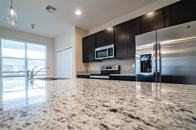 kitchen featuring hanging light fixtures, light stone countertops, sink, and appliances with stainless steel finishes