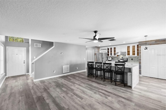 kitchen with appliances with stainless steel finishes, a spacious island, decorative light fixtures, white cabinetry, and a breakfast bar area