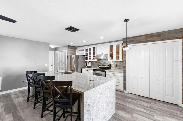 kitchen featuring stainless steel appliances, a kitchen island with sink, sink, pendant lighting, and white cabinetry