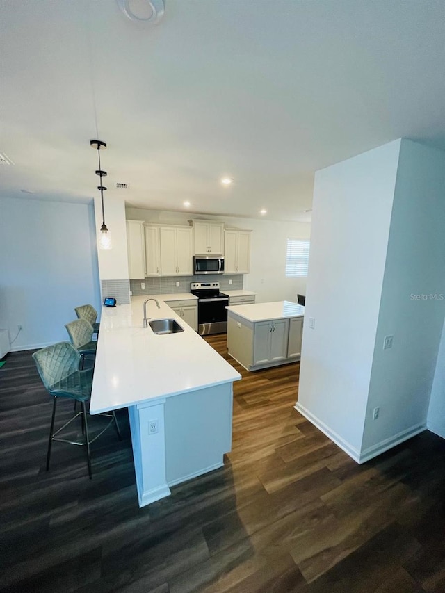 kitchen featuring sink, dark hardwood / wood-style floors, kitchen peninsula, pendant lighting, and appliances with stainless steel finishes