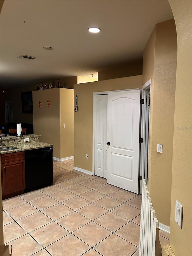 kitchen with light tile patterned flooring, light stone counters, and black dishwasher