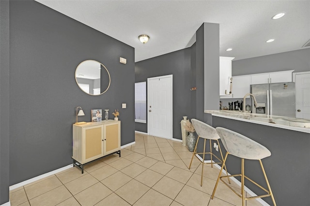 kitchen with a kitchen breakfast bar, white cabinets, light tile patterned flooring, and stainless steel refrigerator with ice dispenser