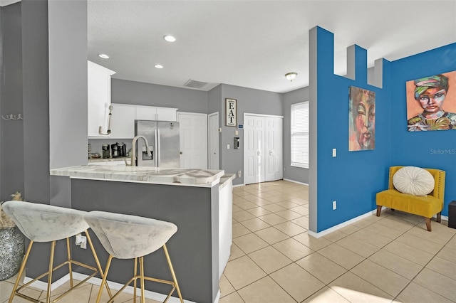 kitchen with white cabinetry, stainless steel refrigerator with ice dispenser, kitchen peninsula, a breakfast bar area, and light tile patterned floors