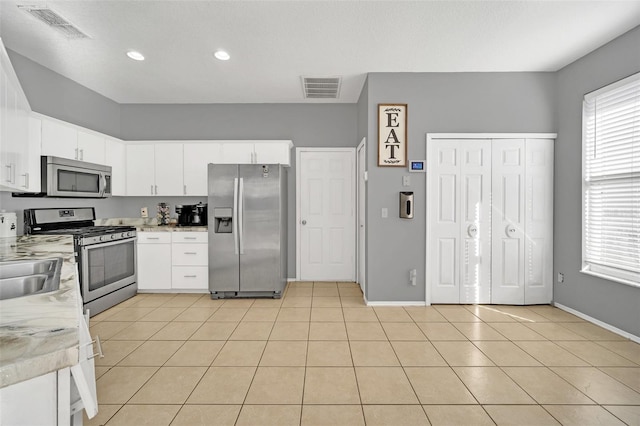 kitchen with light stone countertops, white cabinetry, light tile patterned floors, and stainless steel appliances