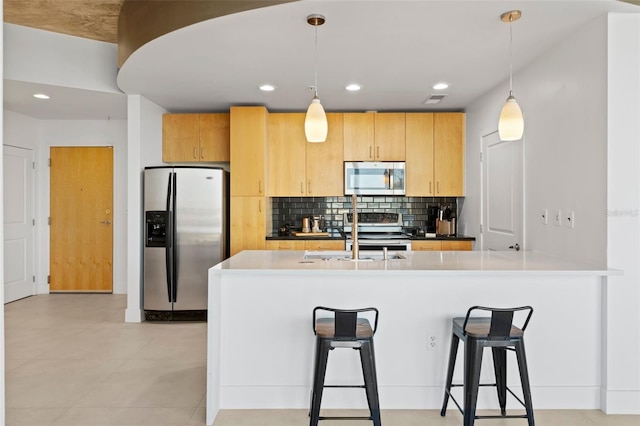 kitchen featuring kitchen peninsula, appliances with stainless steel finishes, sink, light brown cabinets, and hanging light fixtures