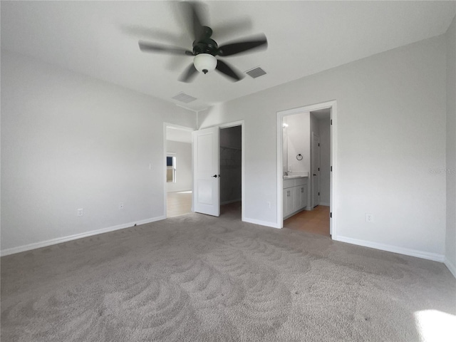 unfurnished bedroom with ceiling fan, light colored carpet, a walk in closet, and connected bathroom