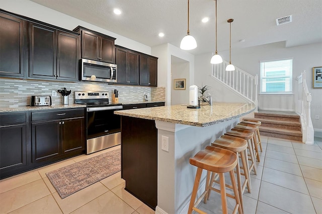 kitchen featuring backsplash, decorative light fixtures, stainless steel appliances, and a kitchen island with sink