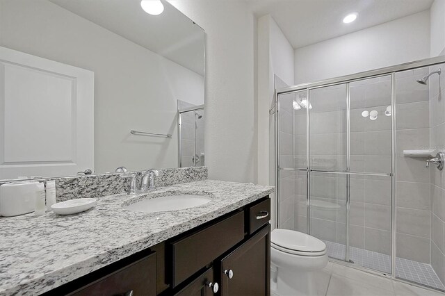 bathroom with an enclosed shower, vanity, toilet, and tile patterned floors