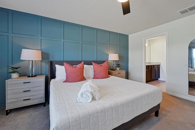 bedroom featuring carpet flooring, a textured ceiling, ensuite bathroom, and ceiling fan