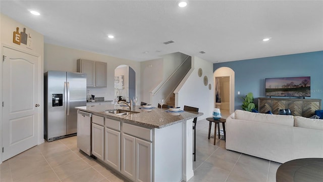 kitchen featuring gray cabinetry, sink, stainless steel appliances, light stone counters, and an island with sink