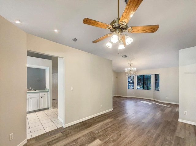 spare room with light hardwood / wood-style flooring, ceiling fan with notable chandelier, and sink