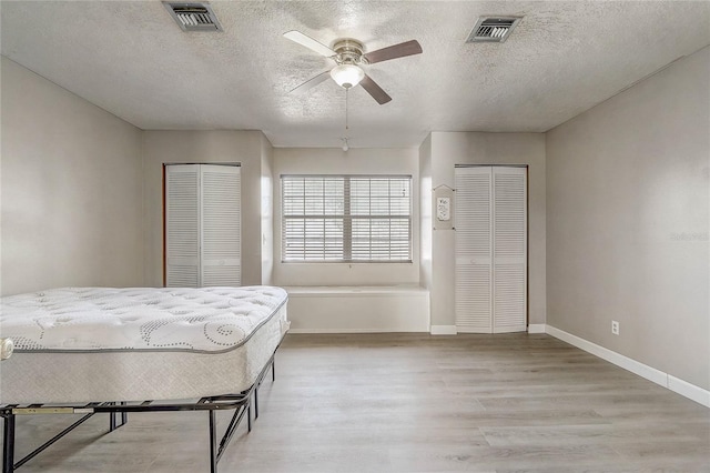 bedroom featuring multiple closets, ceiling fan, light hardwood / wood-style floors, and a textured ceiling