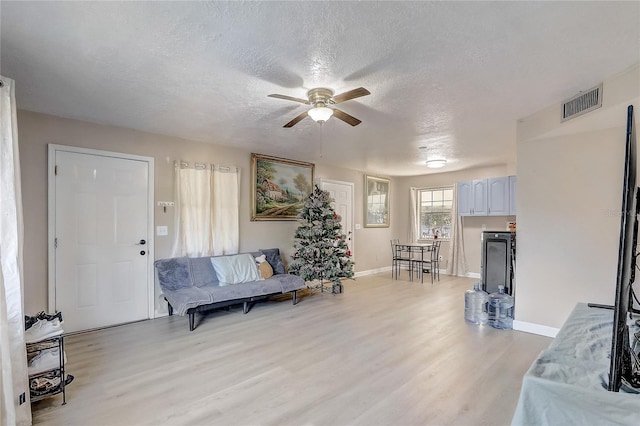 living room featuring a textured ceiling, light wood-type flooring, ceiling fan, baseboards, and visible vents