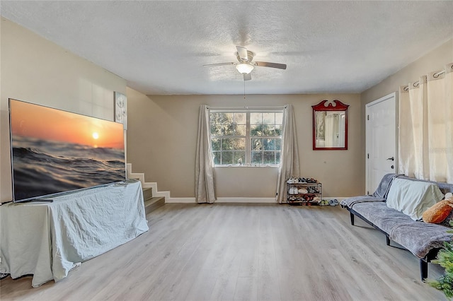 living area featuring stairway, wood finished floors, baseboards, a textured ceiling, and ceiling fan