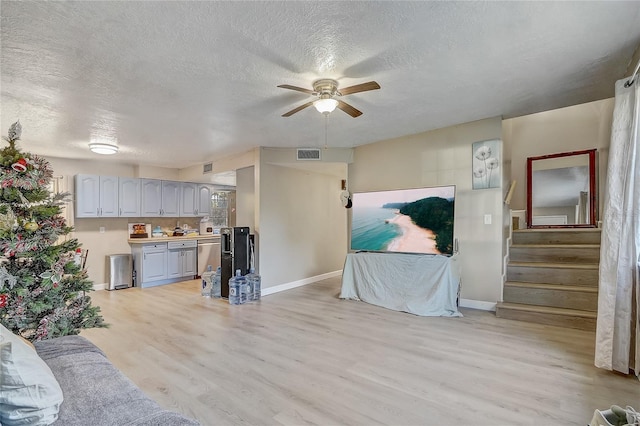 living room with ceiling fan, light wood finished floors, a textured ceiling, and visible vents
