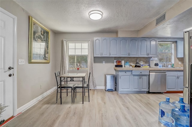 kitchen featuring stainless steel dishwasher, a textured ceiling, visible vents, and light wood-type flooring