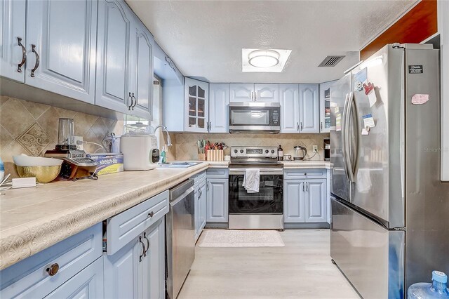 kitchen with stainless steel appliances, tile countertops, a sink, glass insert cabinets, and light wood-style flooring