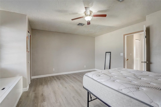 bedroom with a textured ceiling, baseboards, visible vents, light wood-style floors, and a ceiling fan