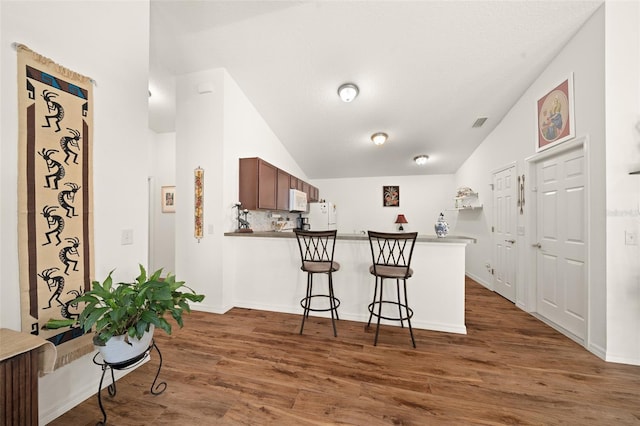 kitchen featuring lofted ceiling, white appliances, kitchen peninsula, and dark wood-type flooring