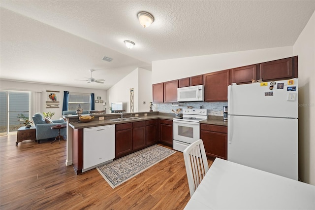 kitchen featuring vaulted ceiling, kitchen peninsula, dark wood-type flooring, and white appliances