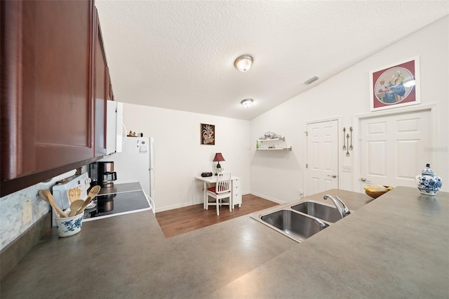 kitchen with stove, a textured ceiling, vaulted ceiling, sink, and white fridge