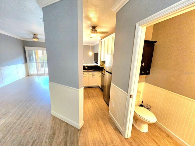 hallway with a textured ceiling, sink, crown molding, and light hardwood / wood-style flooring