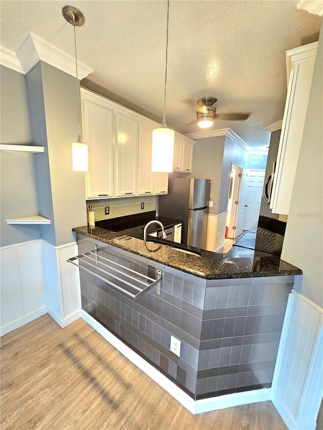 kitchen with hanging light fixtures, light wood-type flooring, ornamental molding, appliances with stainless steel finishes, and white cabinetry