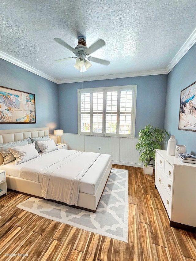 bedroom with ceiling fan, wood-type flooring, a textured ceiling, and ornamental molding