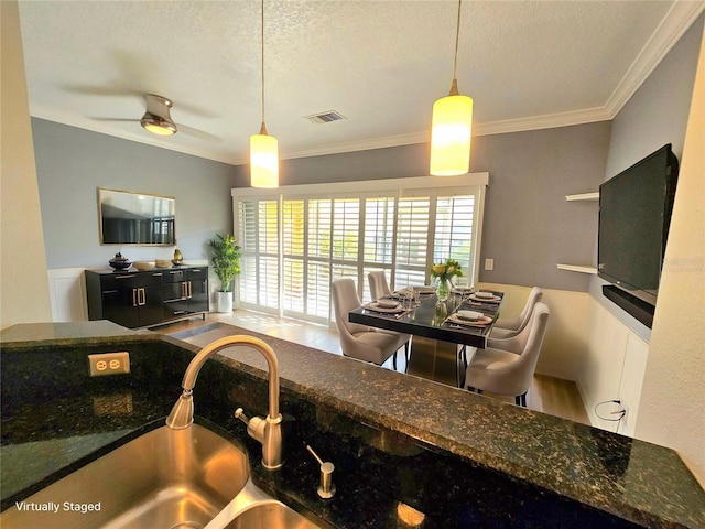 kitchen featuring ceiling fan, sink, crown molding, pendant lighting, and a textured ceiling