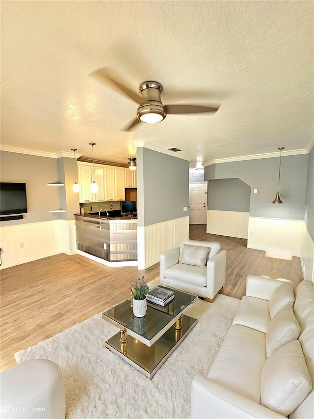 living room featuring sink, hardwood / wood-style flooring, ceiling fan, ornamental molding, and a textured ceiling