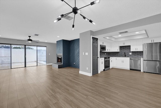 kitchen with ceiling fan, stainless steel appliances, a raised ceiling, white cabinets, and light wood-type flooring