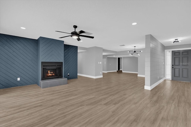 unfurnished living room featuring hardwood / wood-style floors, ceiling fan, a large fireplace, and wooden walls