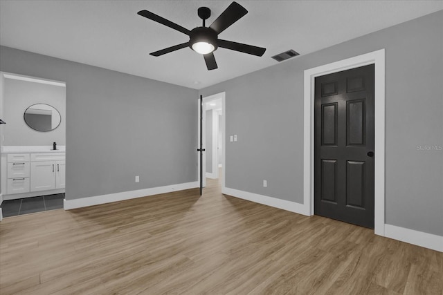 unfurnished bedroom with ceiling fan, light wood-type flooring, sink, and ensuite bath