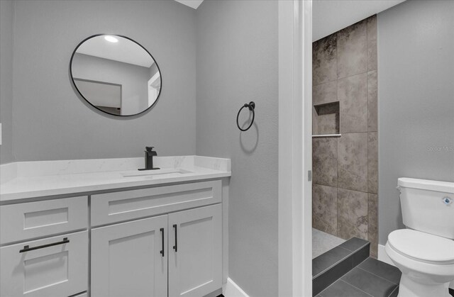 bathroom with a tile shower, vanity, and toilet