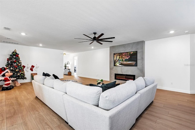 living room with ceiling fan, a large fireplace, a textured ceiling, and light hardwood / wood-style flooring