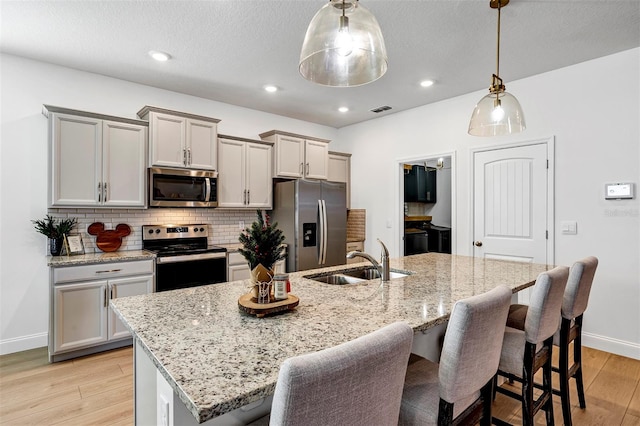 kitchen featuring sink, hanging light fixtures, stainless steel appliances, an island with sink, and light hardwood / wood-style floors