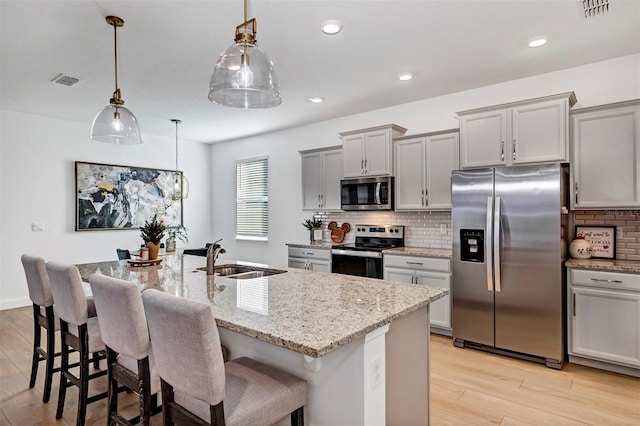 kitchen featuring a center island with sink, sink, light hardwood / wood-style flooring, appliances with stainless steel finishes, and decorative light fixtures