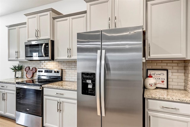 kitchen with light stone countertops, light wood-type flooring, backsplash, and stainless steel appliances