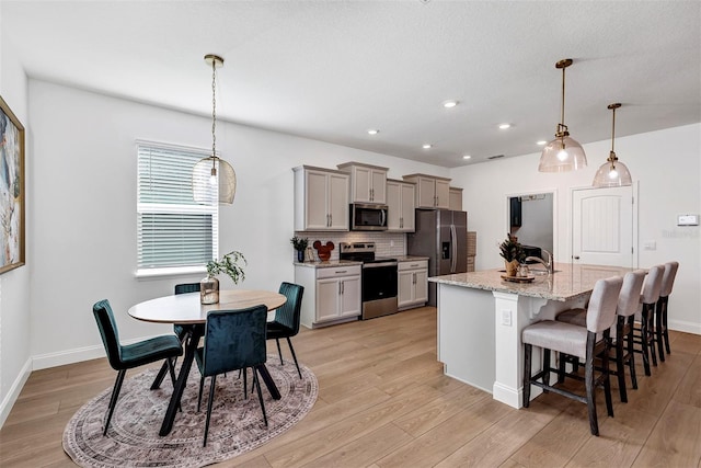 kitchen featuring decorative light fixtures, stainless steel appliances, light hardwood / wood-style flooring, and an island with sink