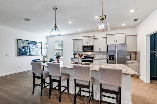 kitchen with stainless steel appliances, pendant lighting, light hardwood / wood-style floors, a kitchen bar, and a center island with sink