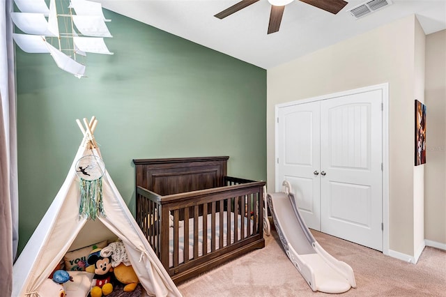 bedroom featuring a crib, a closet, light colored carpet, and ceiling fan